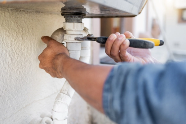 Plumber using a wrench to repair household pipework beneath a sink