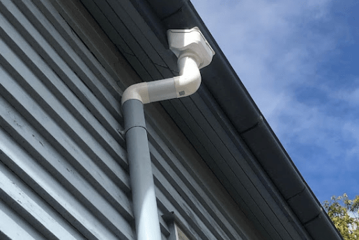 White downpipe connected beneath a residential roof gutter